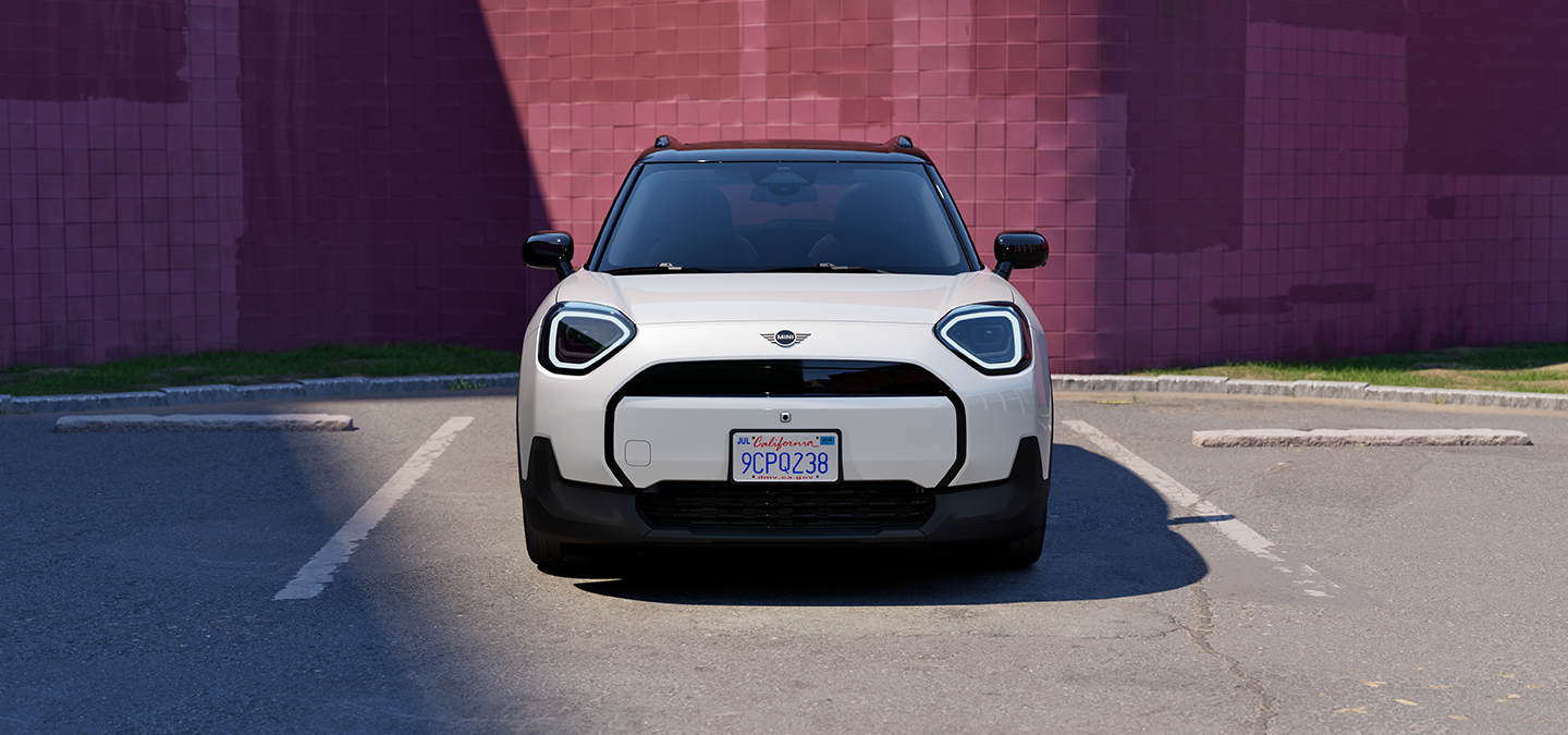 Vista frontale della All-Electric MINI Aceman in Nanuq White con tetto nero, parcheggiata.