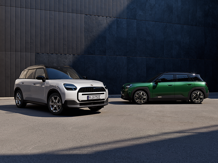Vista frontale e laterale della All-Electric MINI Aceman in Nanuq White e British Racing Green con tetto nero, parcheggiata in strada.