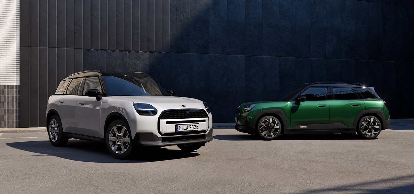 Vista frontale e laterale della All-Electric MINI Aceman in Nanuq White e British Racing Green con tetto nero, parcheggiata in strada.