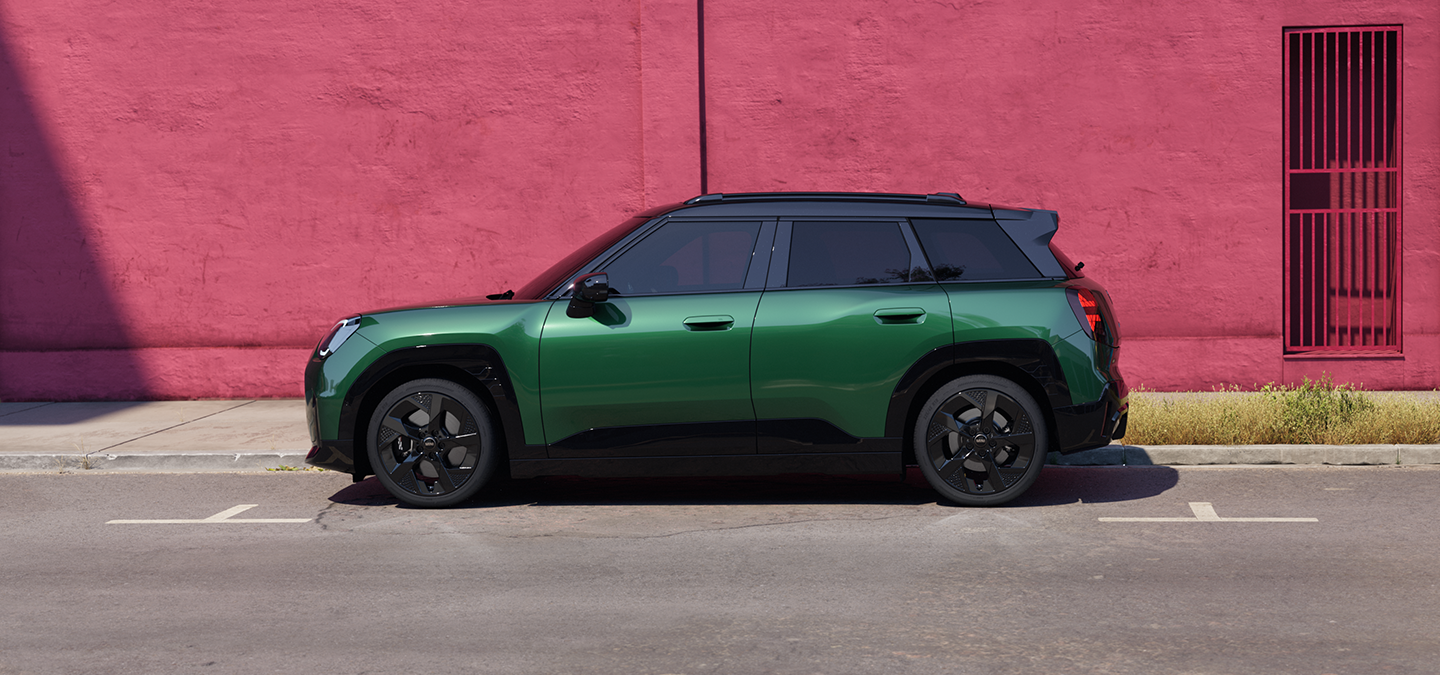 Vista laterale della All-Electric MINI Aceman in British Racing Green con tetto nero, parcheggiata in strada.