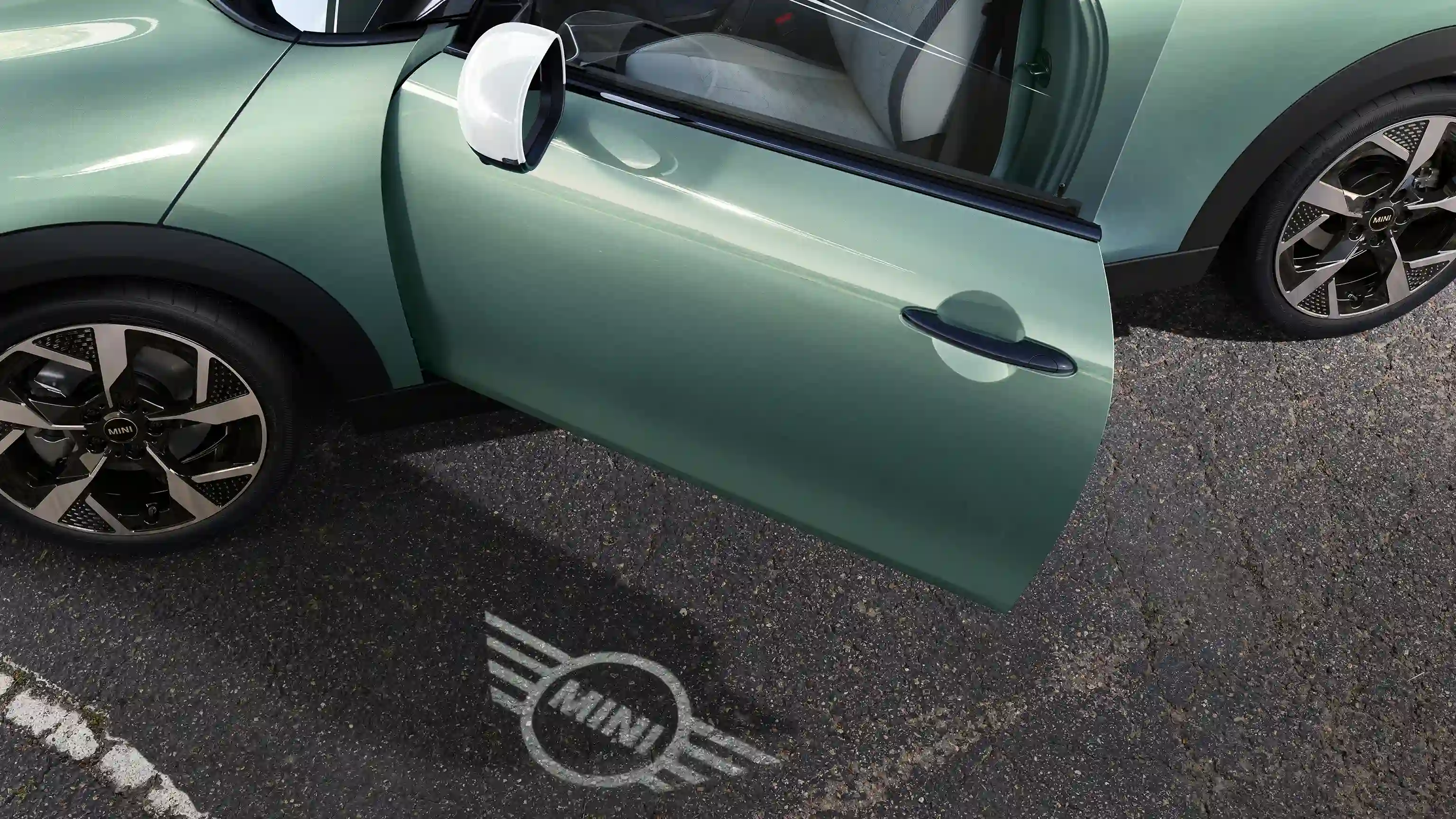 Vue extérieure d’une MINI Cooper avec portière ouverte et projection de bienvenue avec logo MINI sur le sol 