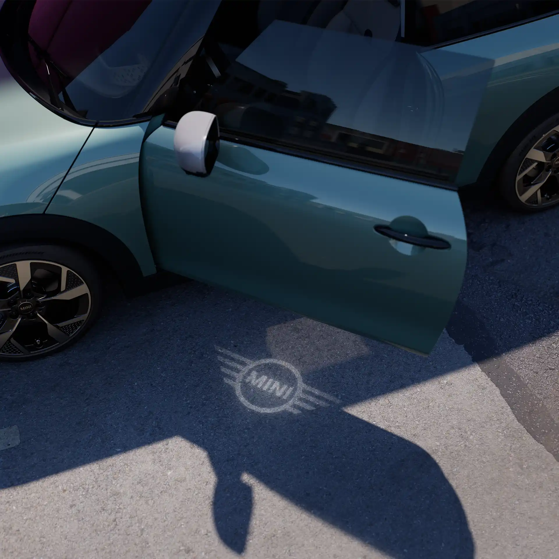 Vista esterna di una MINI Cooper con portiera aperta e luce di benvenuto con logo MINI sul suolo 
