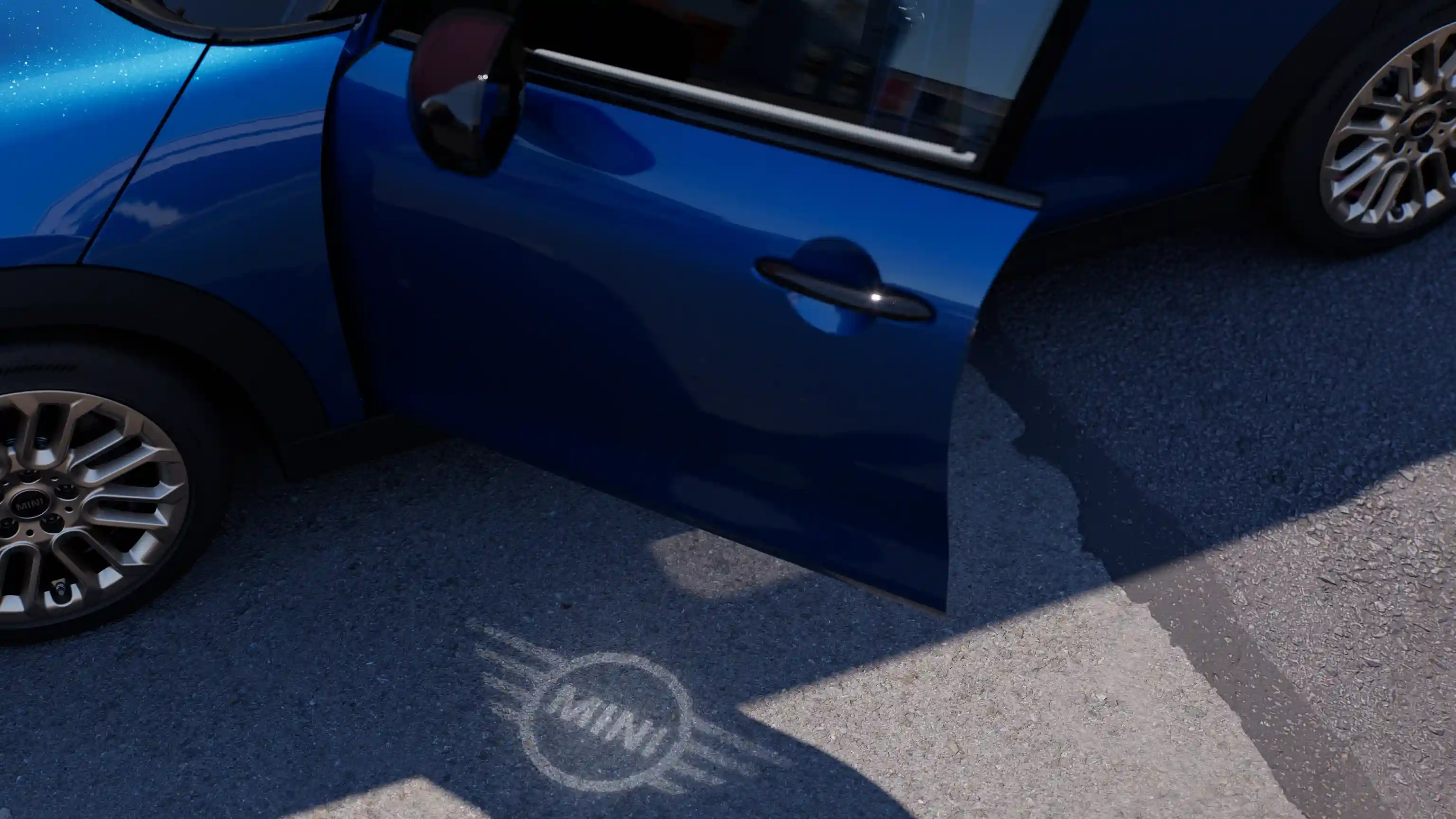 Vista esterna di una MINI Cooper 5 door con portiera aperta e luce di benvenuto con logo MINI sul suolo