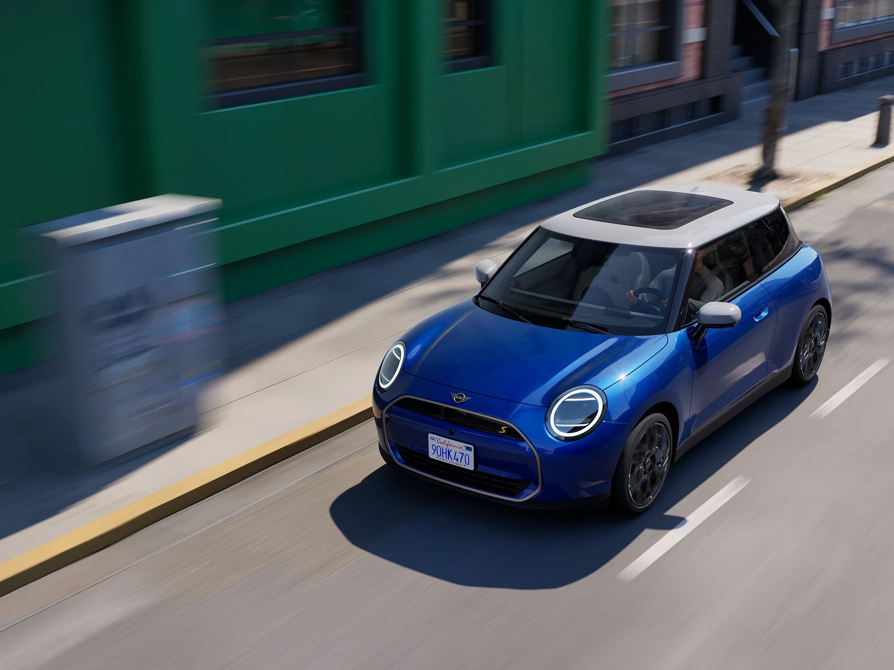 Vue du dessus de la MINI Cooper Electric Blazing Blue avec toit blanc roulant en ville. 