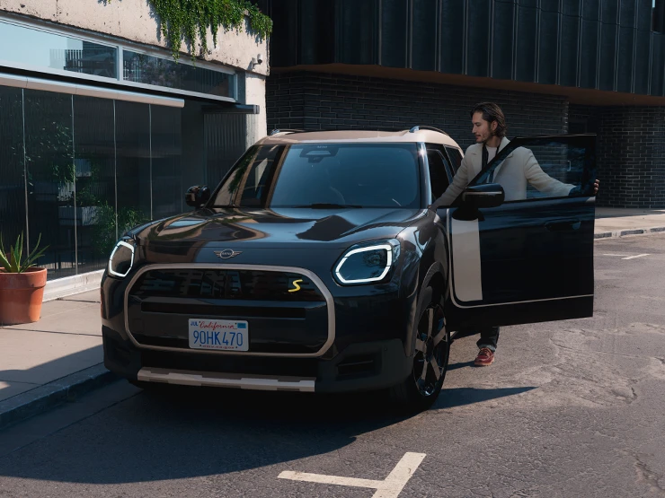 Frontansicht eines vollelektrischen MINI Countryman in Midnight Black mit Dach in Vibrant Silver auf einer Strasse.