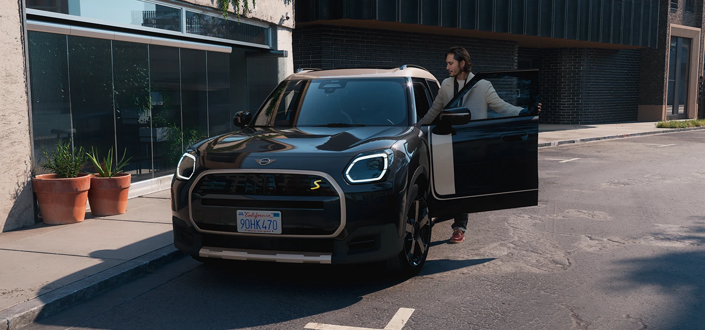 Frontansicht eines vollelektrischen MINI Countryman in Midnight Black mit Dach in Vibrant Silver auf einer Strasse.