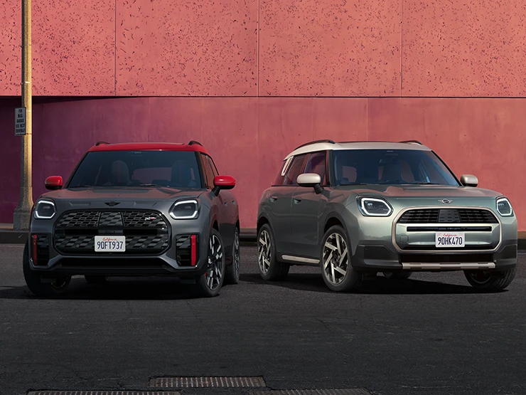 Vue de face du MINI Countryman JCW Legend Grey avec toit rouge et du MINI Countryman Smokey Green avec toit Vibrant Silver stationnés côte-à-côte.