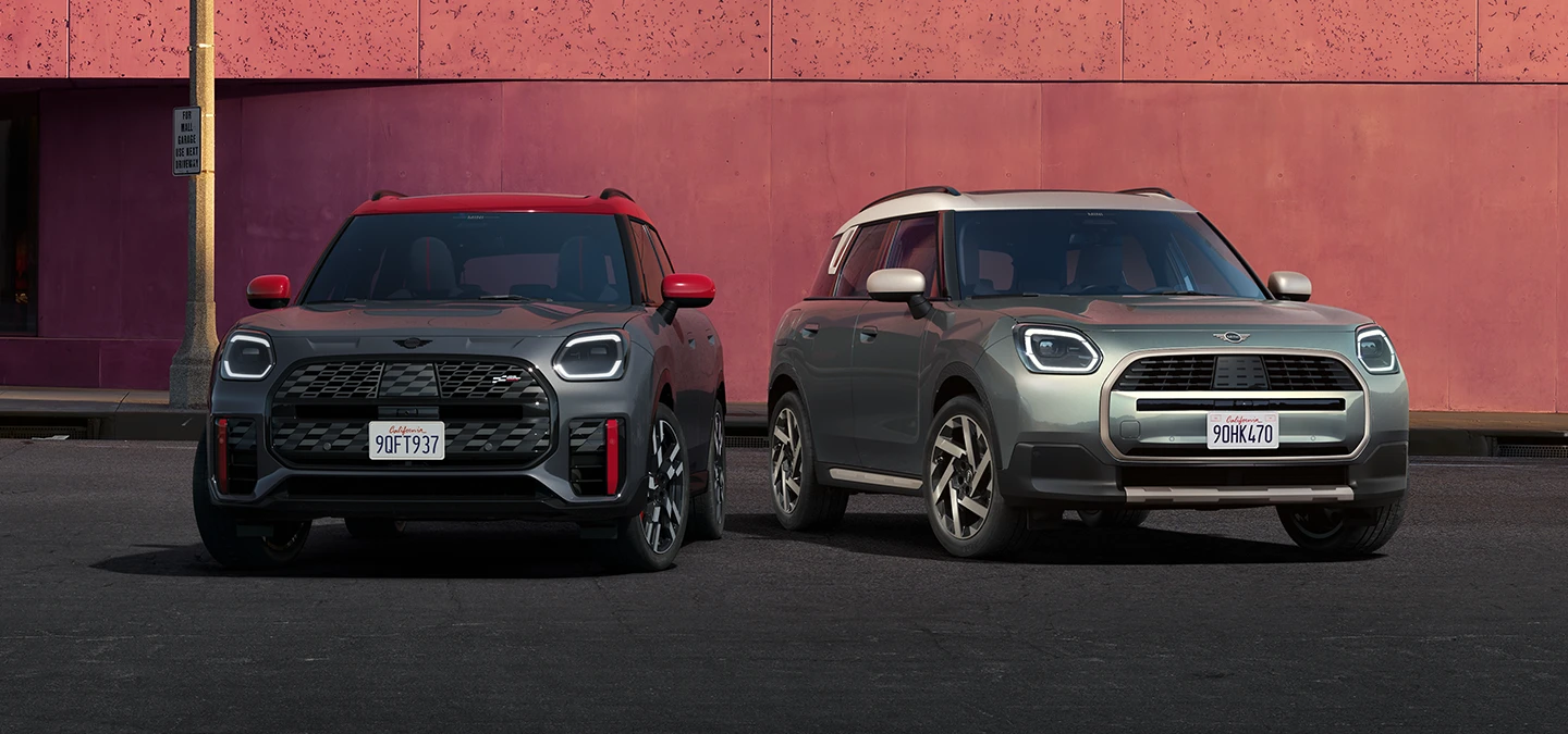 Vue de face du MINI Countryman JCW Legend Grey avec toit rouge et du MINI Countryman Smokey Green avec toit Vibrant Silver stationnés côte-à-côte.