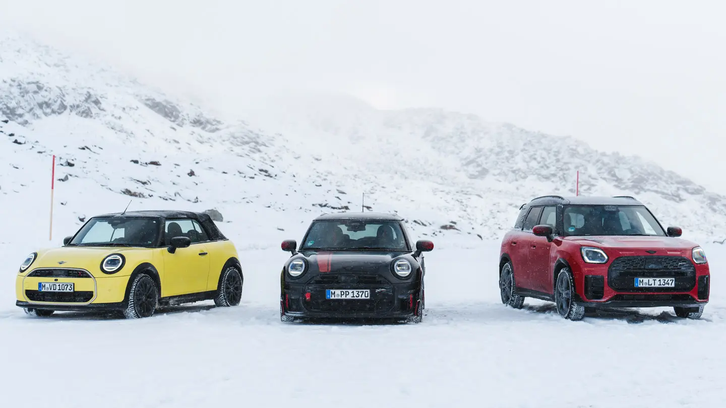 MINI Cooper Cabrio in Sunny Side Yellow, MINI John Cooper Works in Midnight Black II e MINI Countryman Cooper in Chilli Red – ferme su una strada di montagna innevata, vista anteriore.