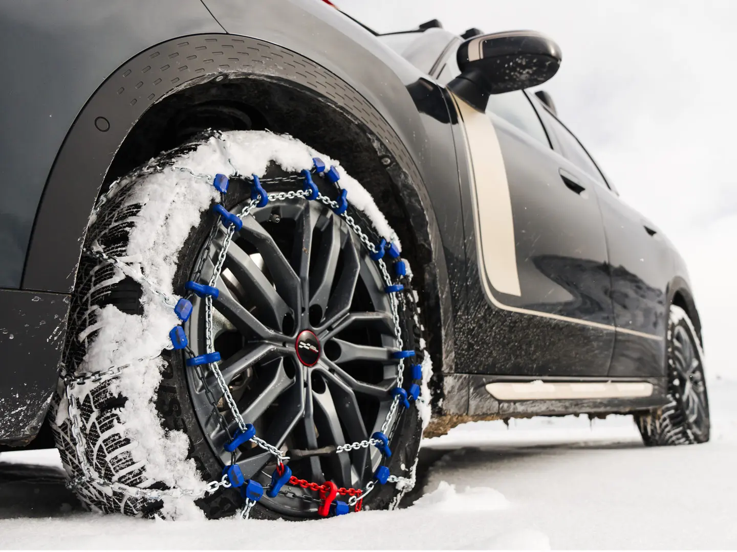 Gros plan d’une chaîne de pneu installée sur la roue d’un MINI Countryman pour une traction accrue lors de la conduite lors de fortes chutes de neige. 