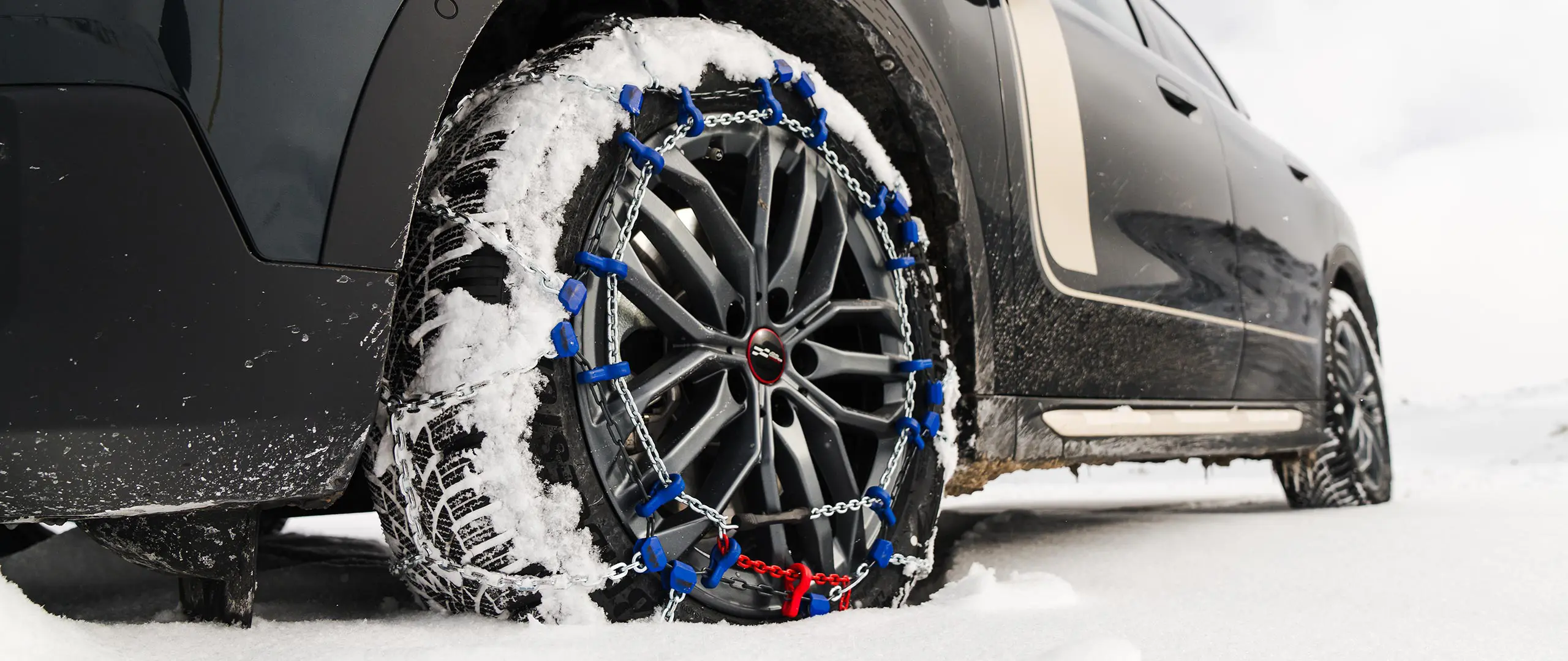 Gros plan d’une chaîne de pneu installée sur la roue d’un MINI Countryman pour une traction accrue lors de la conduite lors de fortes chutes de neige. 