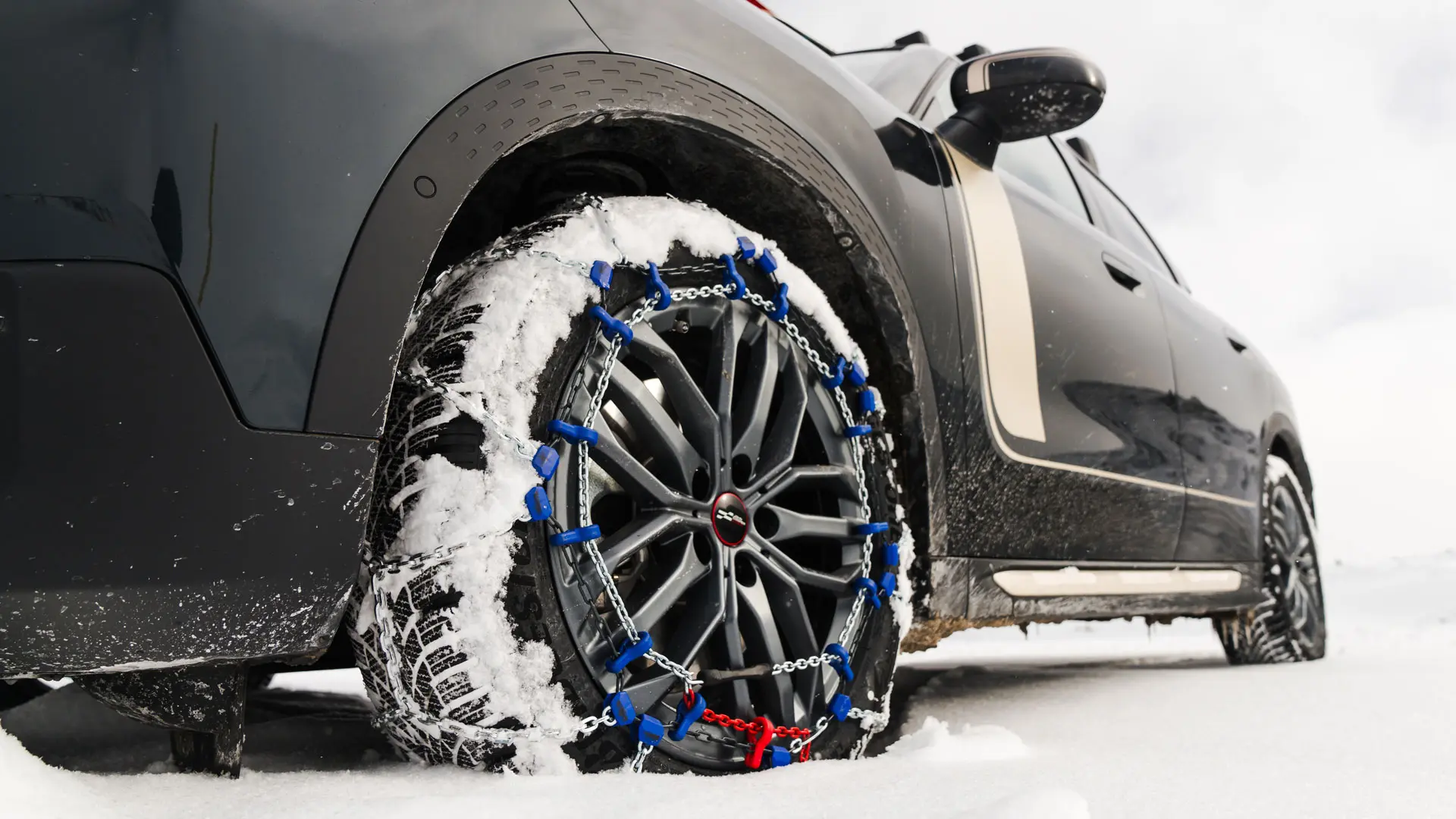 Gros plan d’une chaîne de pneu installée sur la roue d’un MINI Countryman pour une traction accrue lors de la conduite lors de fortes chutes de neige. 