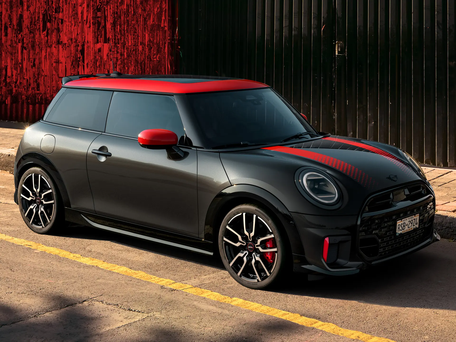 Seitenansicht eines MINI John Cooper Works 3-Türer in Midnight Black mit Dach und Spiegelkappen in Chili Red und roten Seitenstreifen, der am Strassenrand parkiert ist.
