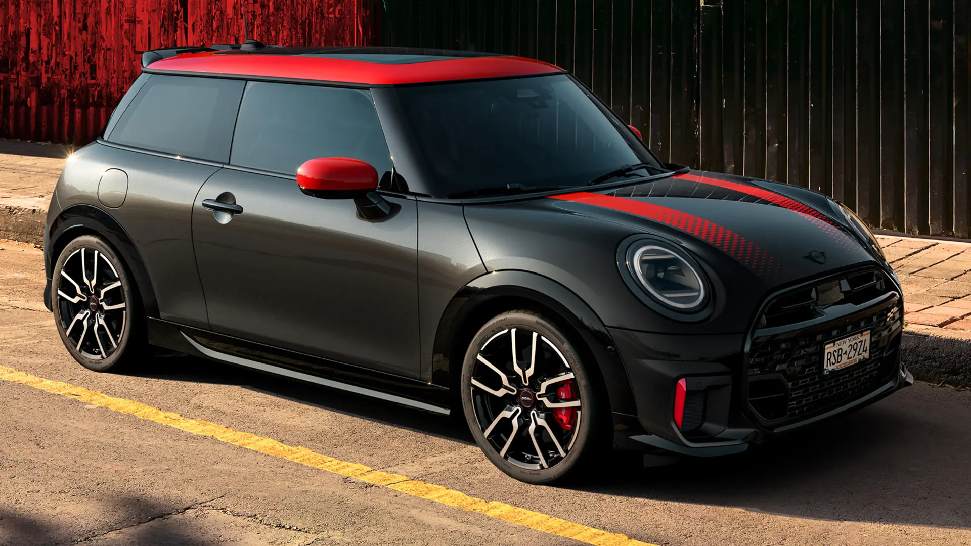 Seitenansicht eines MINI John Cooper Works 3-Türer in Midnight Black mit Dach und Spiegelkappen in Chili Red und roten Seitenstreifen, der am Strassenrand parkiert ist.
