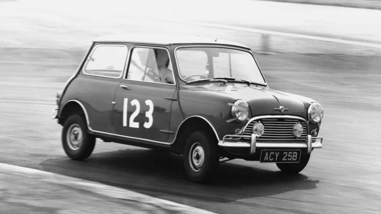  Lächelnde Menschen stehen um einen alten MINI Racer MK1 Trackside, ein Mann sitzt im MINI und versucht vorbei zu fahren