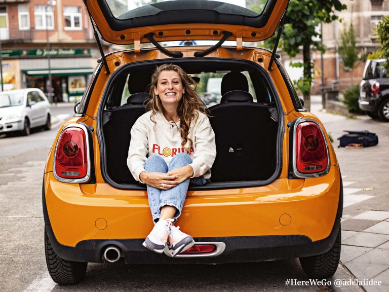 MINI 3-Türer Hatch in Volcanic Orange mit glücklicher Frau, die im Kofferraum sitzt