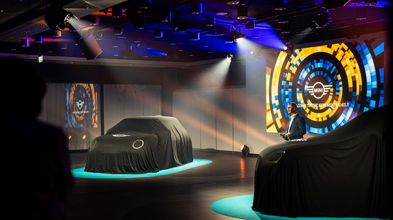 Due MINI sul palco coperte da un telo e illuminate da riflettori Due MINI sul palco coperte da un telo nero e illuminate da riflettori