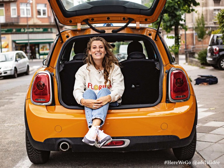 MINI 3 porte in Volcanic Orange con una donna felice seduta sul portabagagli